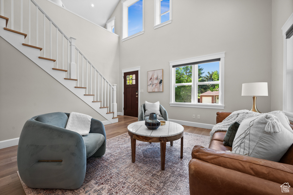 Living area featuring plenty of natural light, a towering ceiling, stairs, baseboards, and wood finished floors