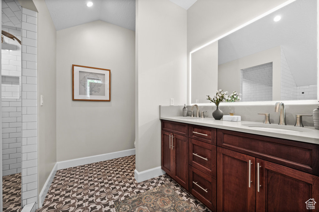 Full bath featuring double vanity, lofted ceiling, tiled shower, baseboards, and recessed lighting