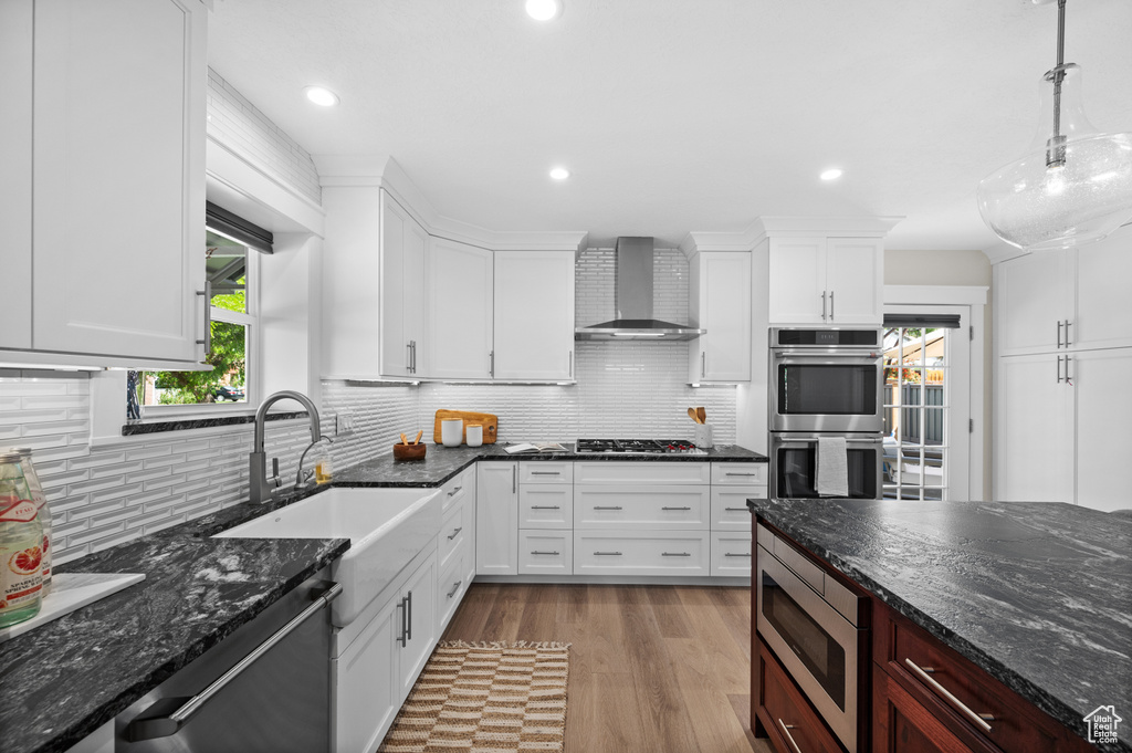 Kitchen with wall chimney range hood, appliances with stainless steel finishes, a sink, white cabinets, and recessed lighting