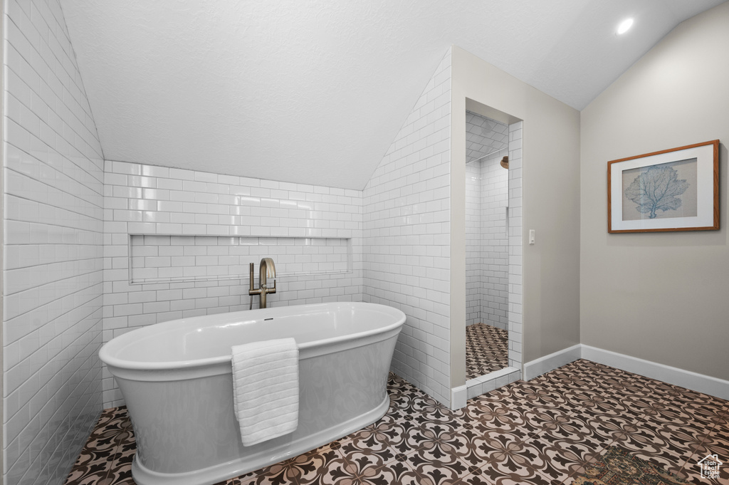 Bathroom with lofted ceiling, tile walls, a soaking tub, and a stall shower