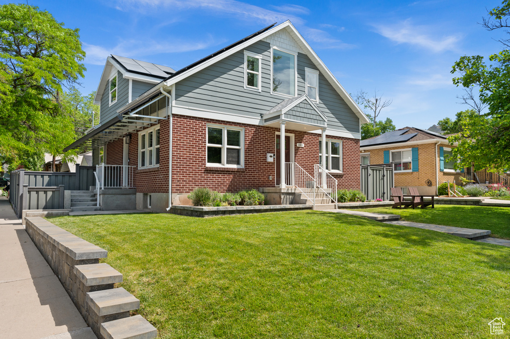 Bungalow-style home with brick siding, a front lawn, and solar panels