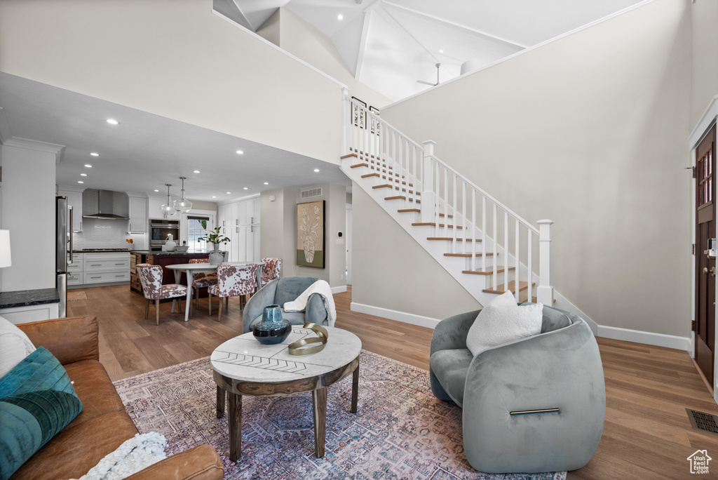 Living room with light wood-type flooring, stairway, baseboards, recessed lighting, and a towering ceiling