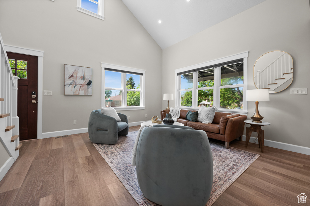 Living area with stairs, high vaulted ceiling, plenty of natural light, wood finished floors, and recessed lighting
