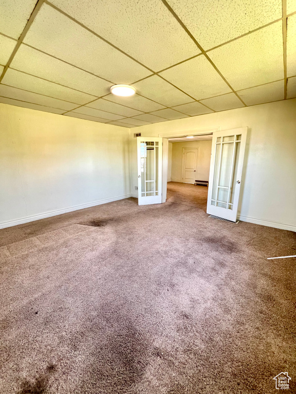 Carpeted empty room featuring a drop ceiling, french doors, baseboards, and a baseboard radiator