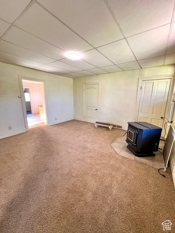 Carpeted spare room with a wood stove, a paneled ceiling, and baseboards