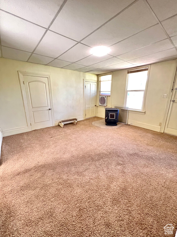 Empty room with a wood stove, a drop ceiling, carpet, baseboards, and cooling unit