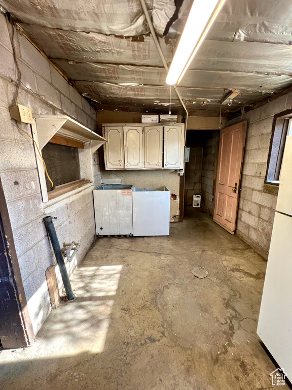 Unfinished below grade area featuring freestanding refrigerator, concrete block wall, and fridge
