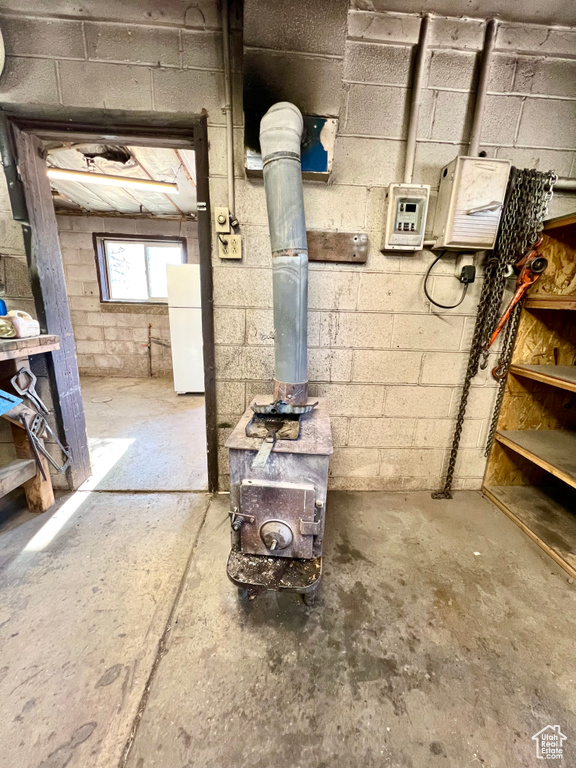 Basement featuring freestanding refrigerator, a wood stove, and concrete block wall