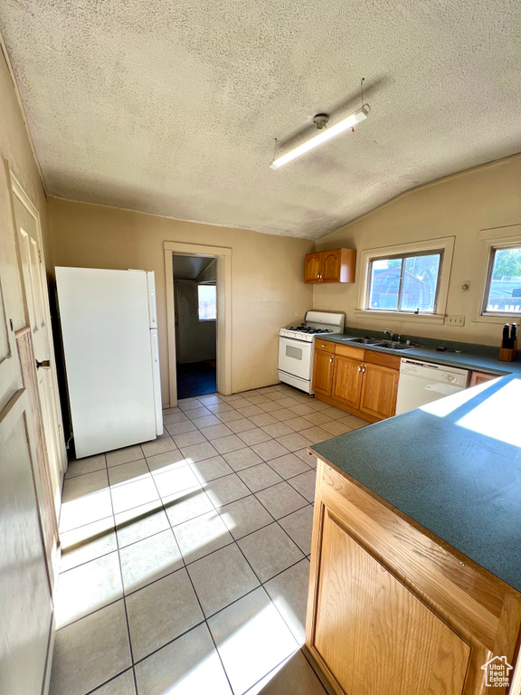 Kitchen featuring white appliances, a sink, dark countertops, a textured ceiling, and light tile patterned floors