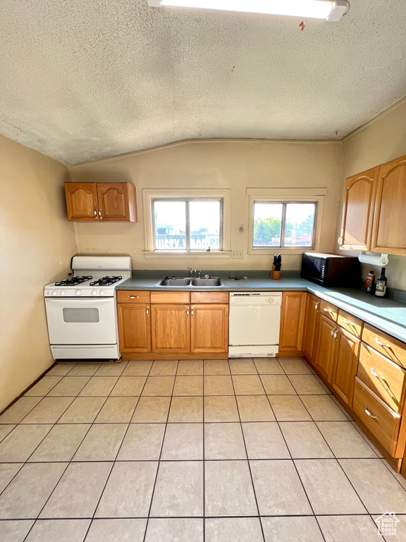 Kitchen with white appliances, a sink, a textured ceiling, vaulted ceiling, and light tile patterned flooring