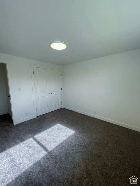 Unfurnished bedroom featuring dark carpet, baseboards, and a closet