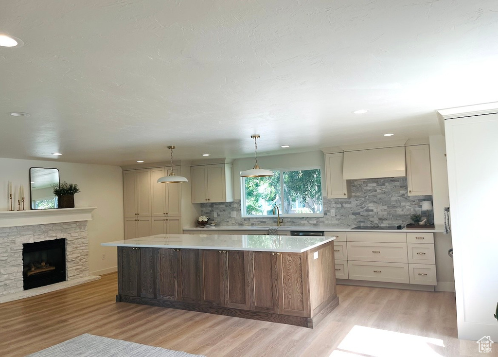 Kitchen with light wood-style floors, a center island, tasteful backsplash, a fireplace, and custom exhaust hood