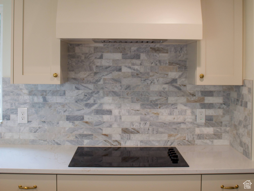 Kitchen with custom range hood, light countertops, white cabinets, backsplash, and black electric cooktop