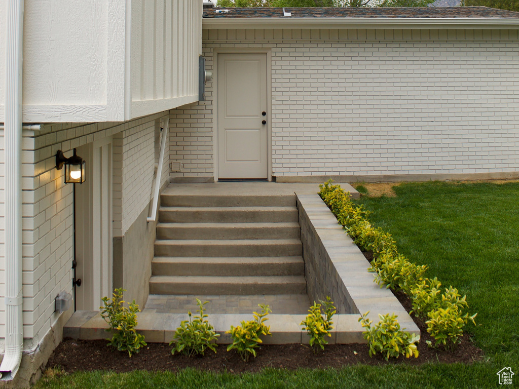 View of exterior entry with brick siding and a yard