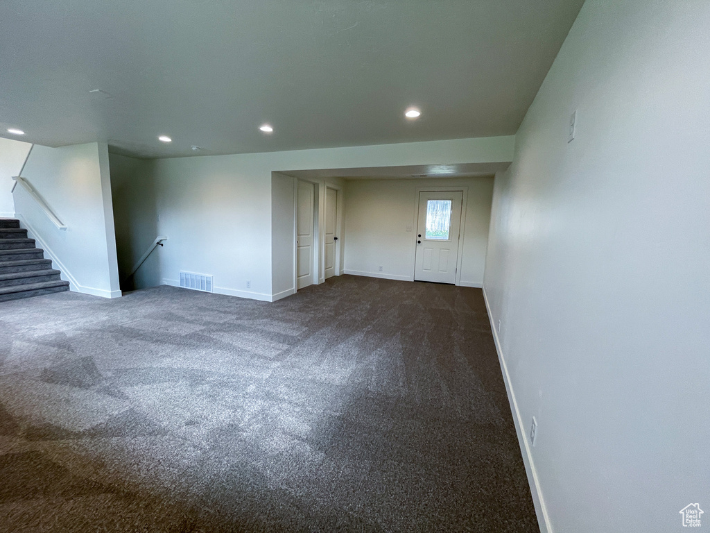 Unfurnished room featuring dark carpet, baseboards, recessed lighting, and stairway