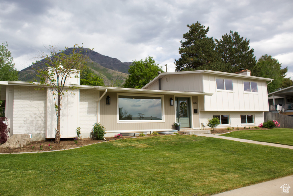 Tri-level home with brick siding, a chimney, a front lawn, and a mountain view