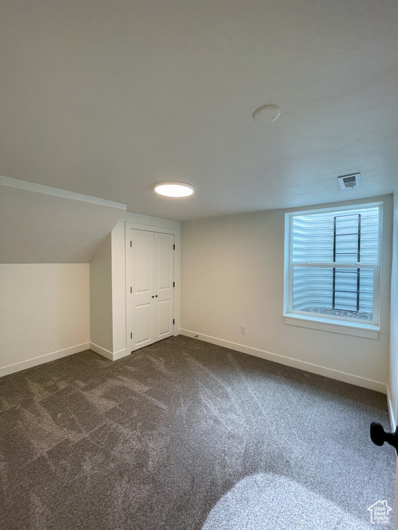 Bonus room featuring dark colored carpet and baseboards