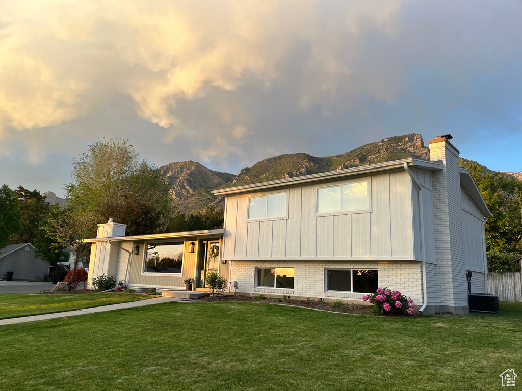 Tri-level home featuring a chimney, a mountain view, a front lawn, board and batten siding, and brick siding