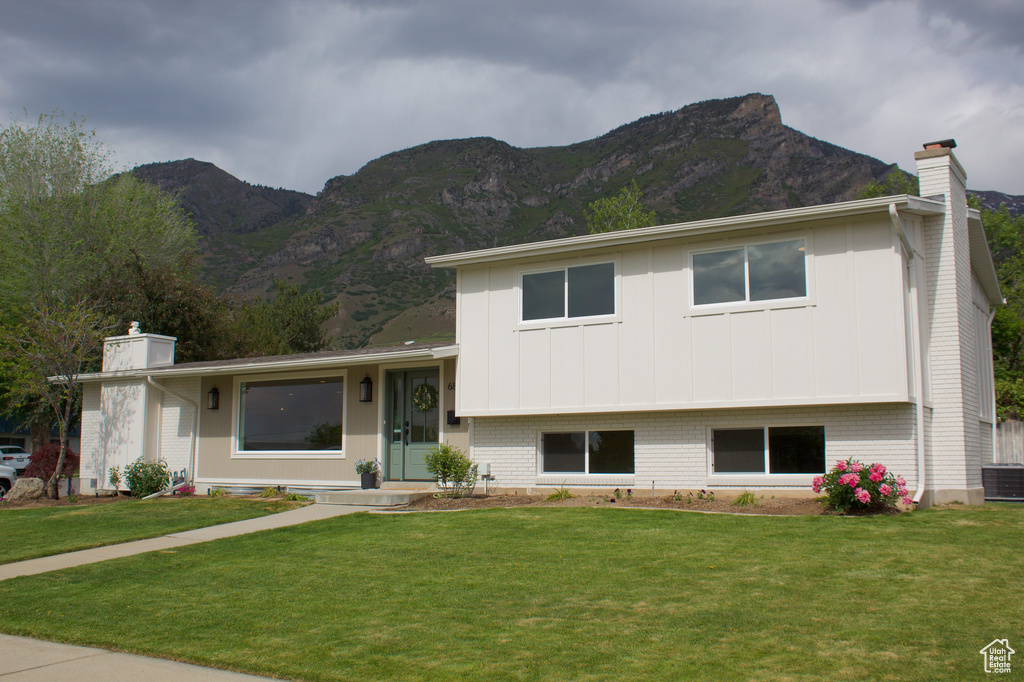 Tri-level home featuring a chimney, a mountain view, a front lawn, board and batten siding, and brick siding