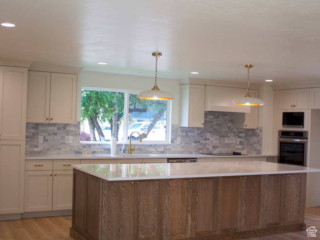 Kitchen featuring stainless steel oven, a sink, light wood-type flooring, a kitchen island, and light countertops