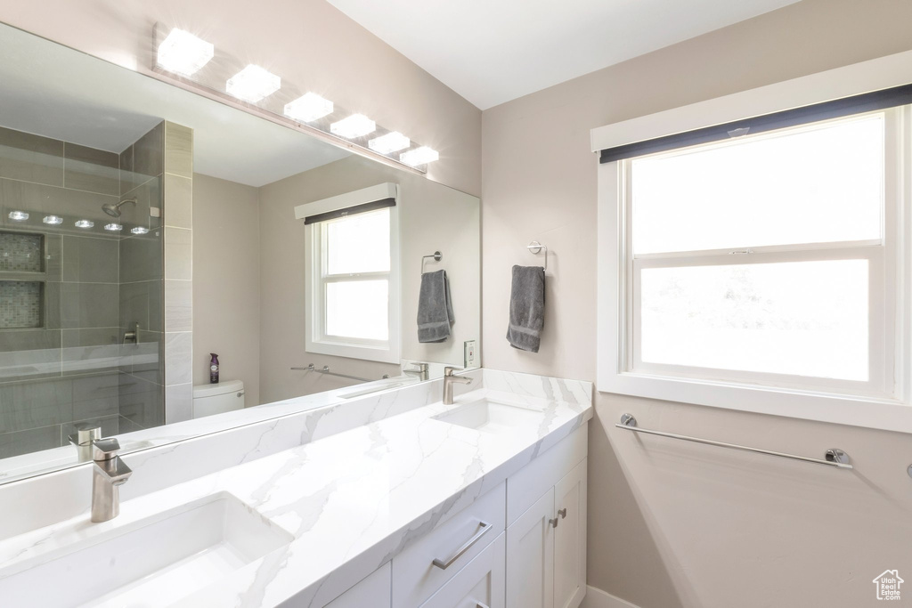 Full bathroom featuring double vanity, tiled shower, and toilet