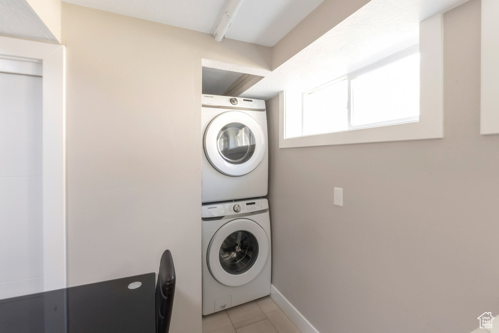 Laundry room featuring stacked washer / dryer, light tile patterned floors, and baseboards