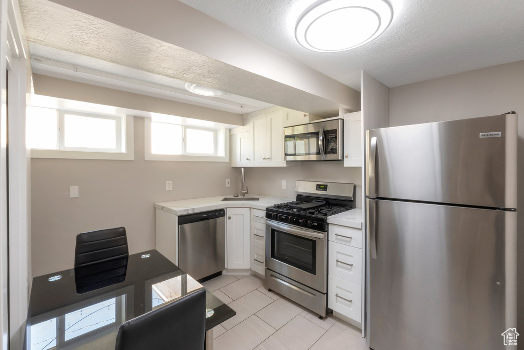 Kitchen with appliances with stainless steel finishes, light countertops, white cabinets, light tile patterned floors, and a sink
