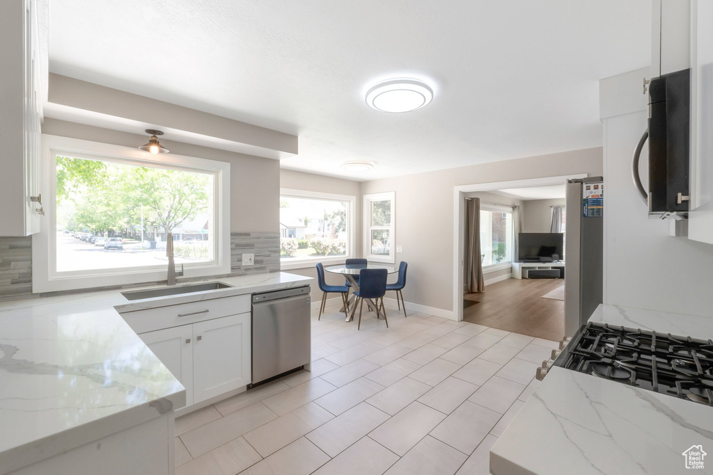 Kitchen featuring stainless steel dishwasher, black microwave, a sink, tasteful backsplash, and light stone counters