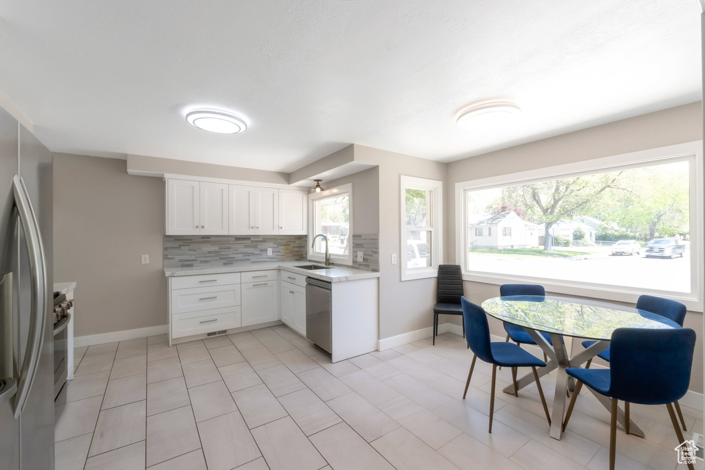 Kitchen with stainless steel appliances, light countertops, backsplash, a sink, and baseboards