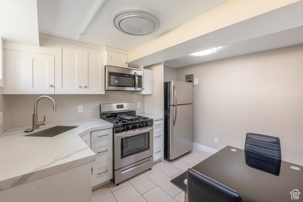 Kitchen with appliances with stainless steel finishes, a sink, white cabinetry, light tile patterned floors, and light stone counters