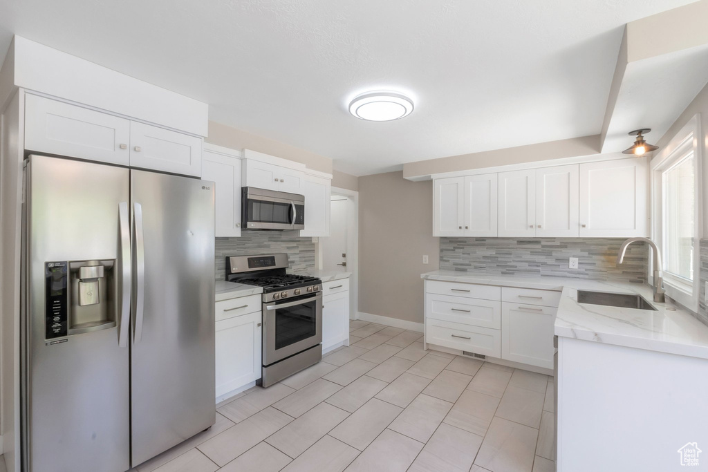 Kitchen featuring appliances with stainless steel finishes, a sink, decorative backsplash, white cabinets, and light stone counters