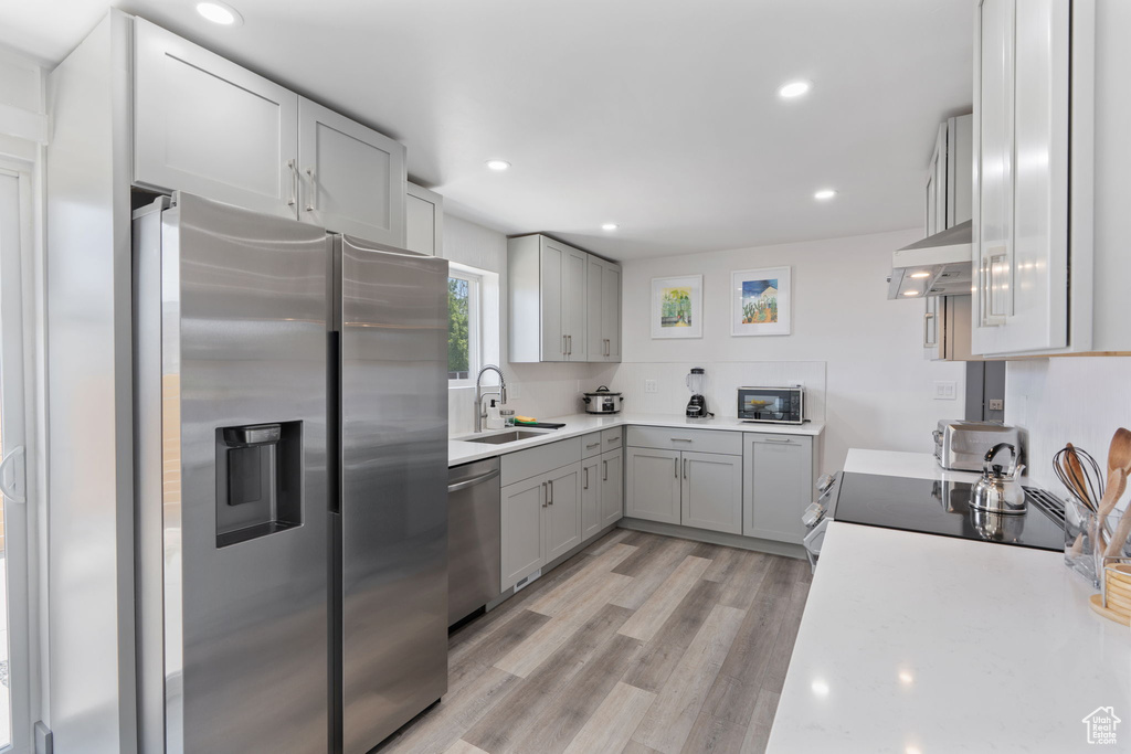 Kitchen with stainless steel appliances, a sink, under cabinet range hood, light countertops, and gray cabinets