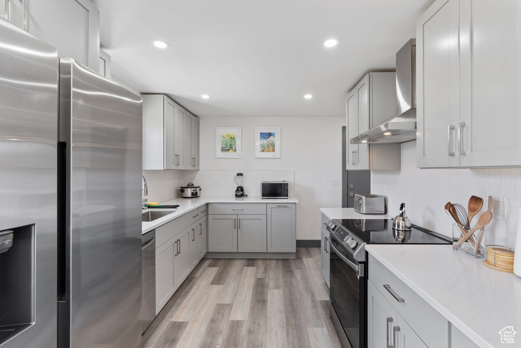 Kitchen featuring stainless steel appliances, wall chimney range hood, a sink, light wood-style floors, and light countertops