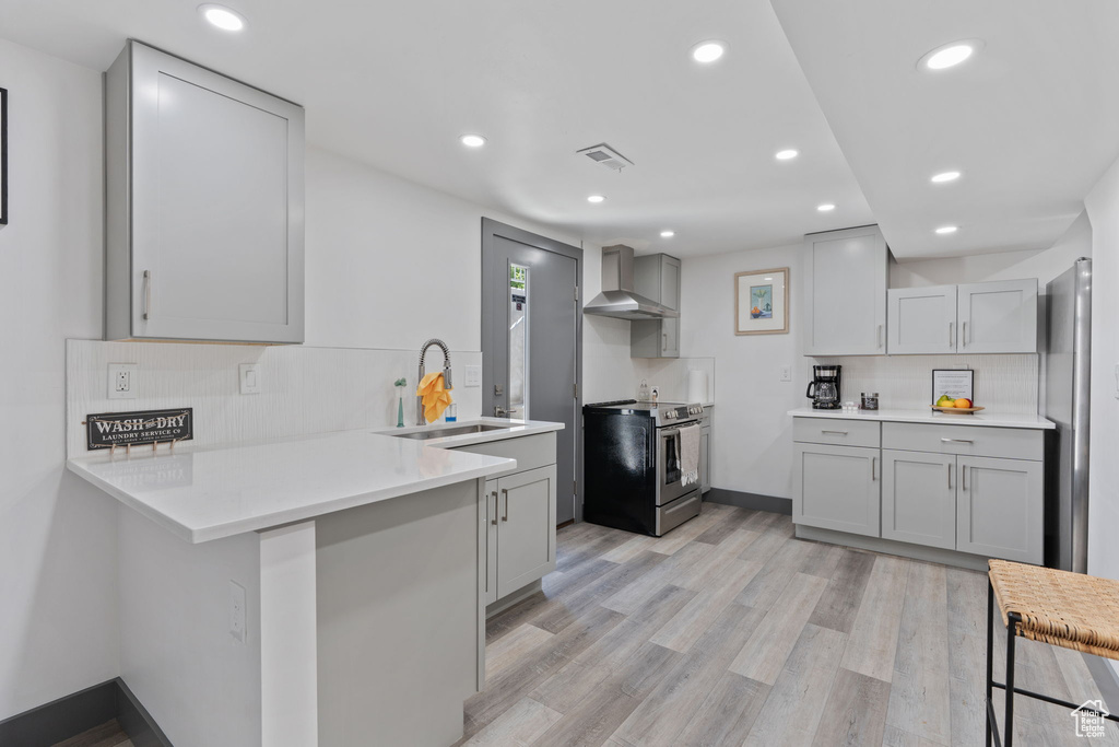 Kitchen with electric range, wall chimney range hood, a sink, a peninsula, and gray cabinetry