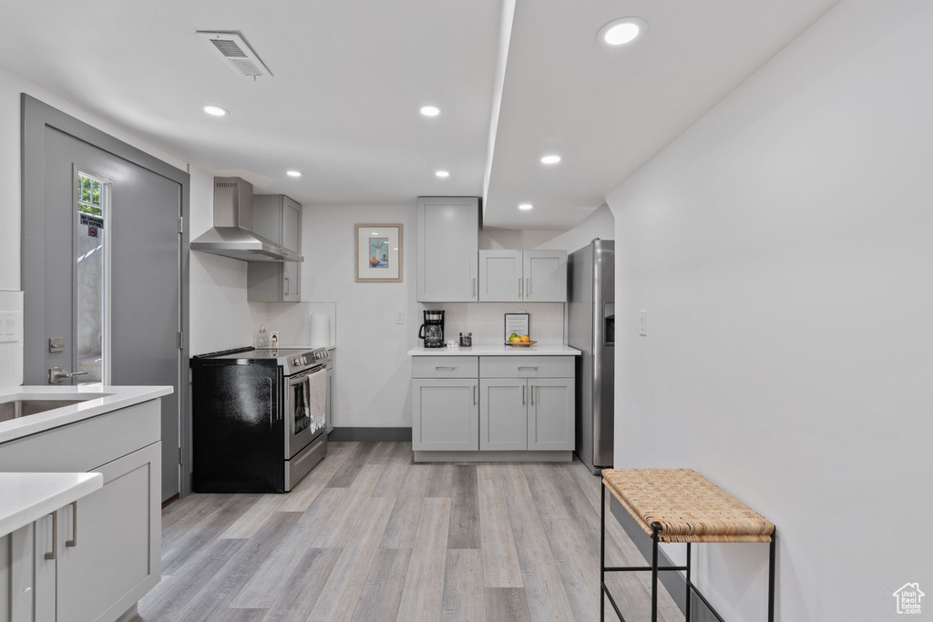 Kitchen featuring stainless steel appliances, wall chimney range hood, light wood-style flooring, light countertops, and gray cabinets