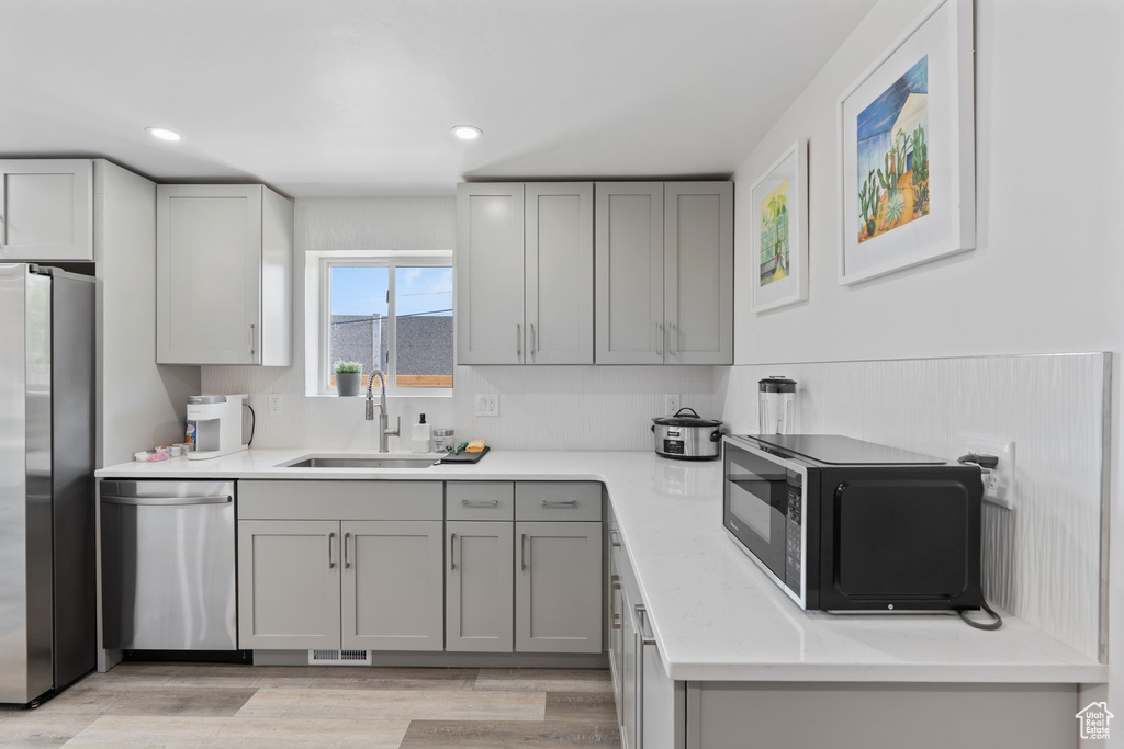 Kitchen with appliances with stainless steel finishes, a sink, gray cabinets, light countertops, and recessed lighting