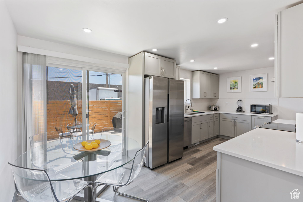 Kitchen with appliances with stainless steel finishes, gray cabinets, light wood-type flooring, a sink, and recessed lighting