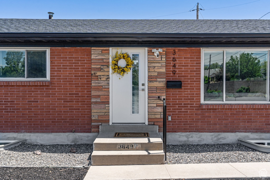 View of exterior entry with brick siding and roof with shingles