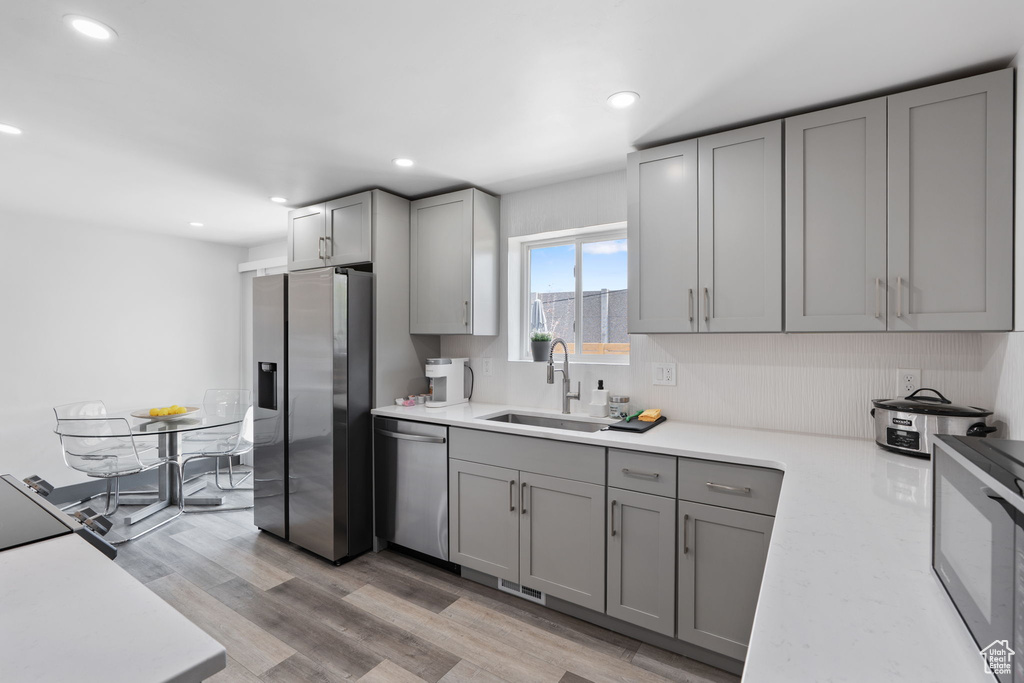Kitchen featuring stainless steel appliances, a sink, gray cabinets, light countertops, and light wood-type flooring