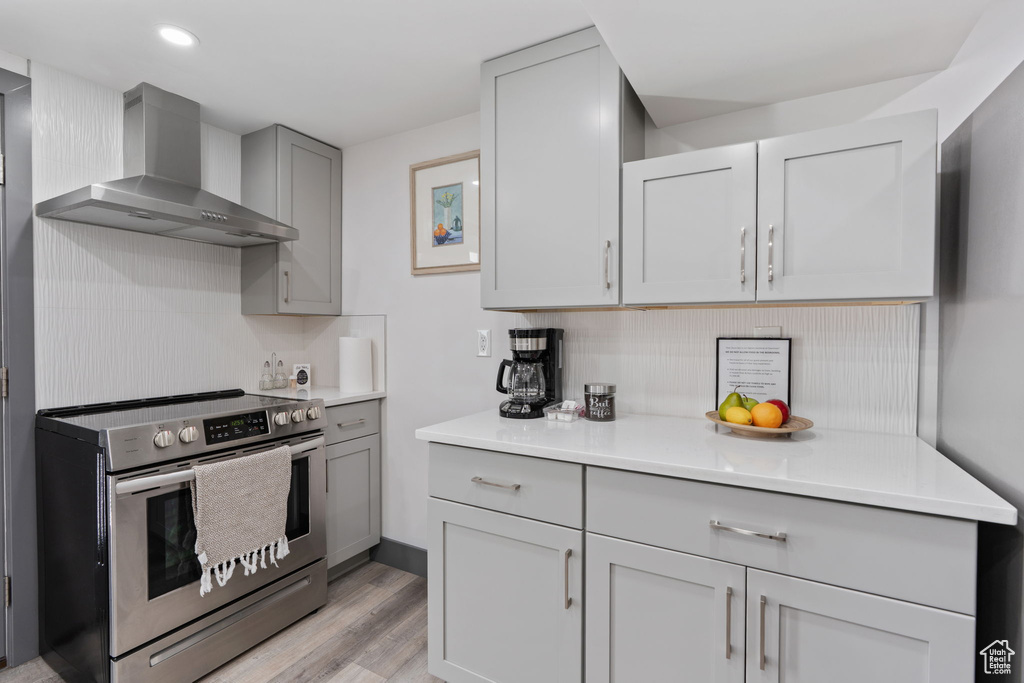 Kitchen with electric range, wall chimney range hood, gray cabinetry, light wood-style floors, and light countertops