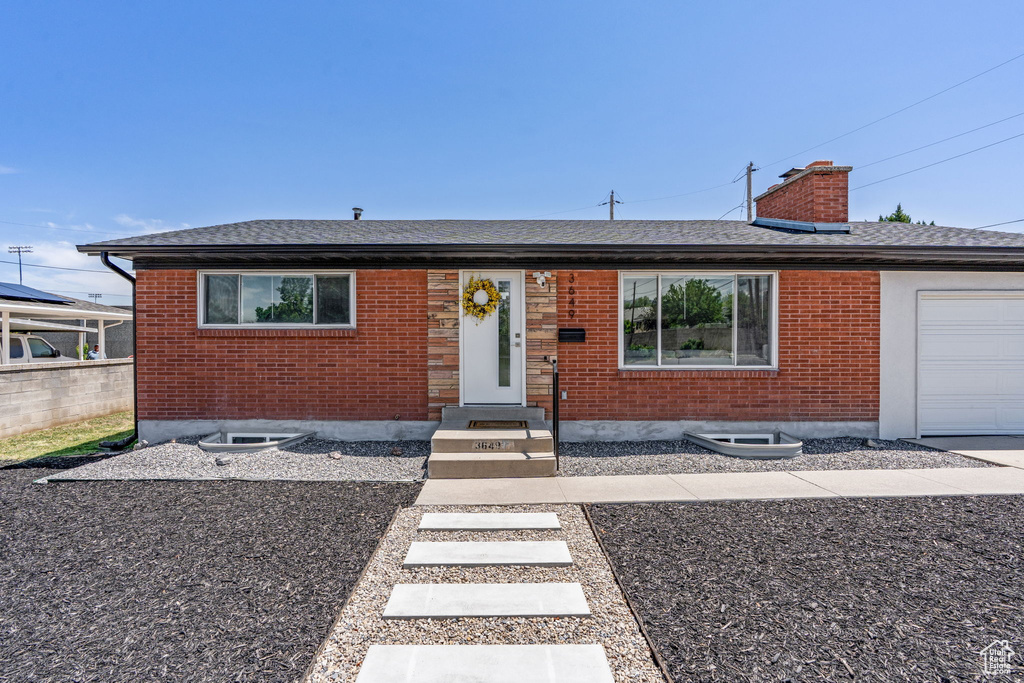View of front of property featuring an attached garage, brick siding, roof with shingles, and a chimney