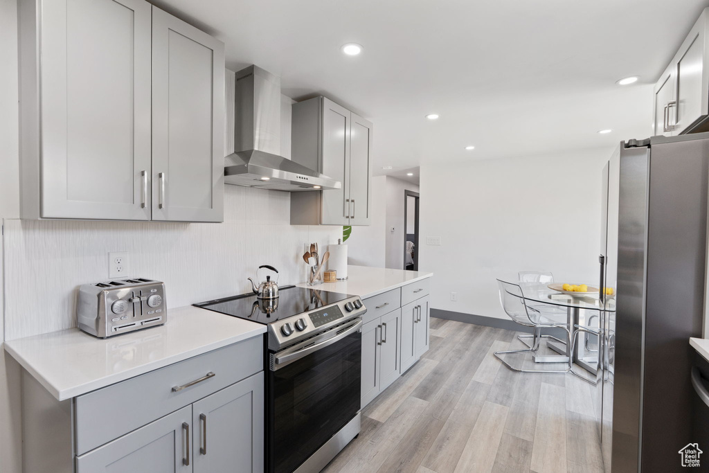 Kitchen with wall chimney range hood, stainless steel appliances, decorative backsplash, gray cabinets, and light countertops