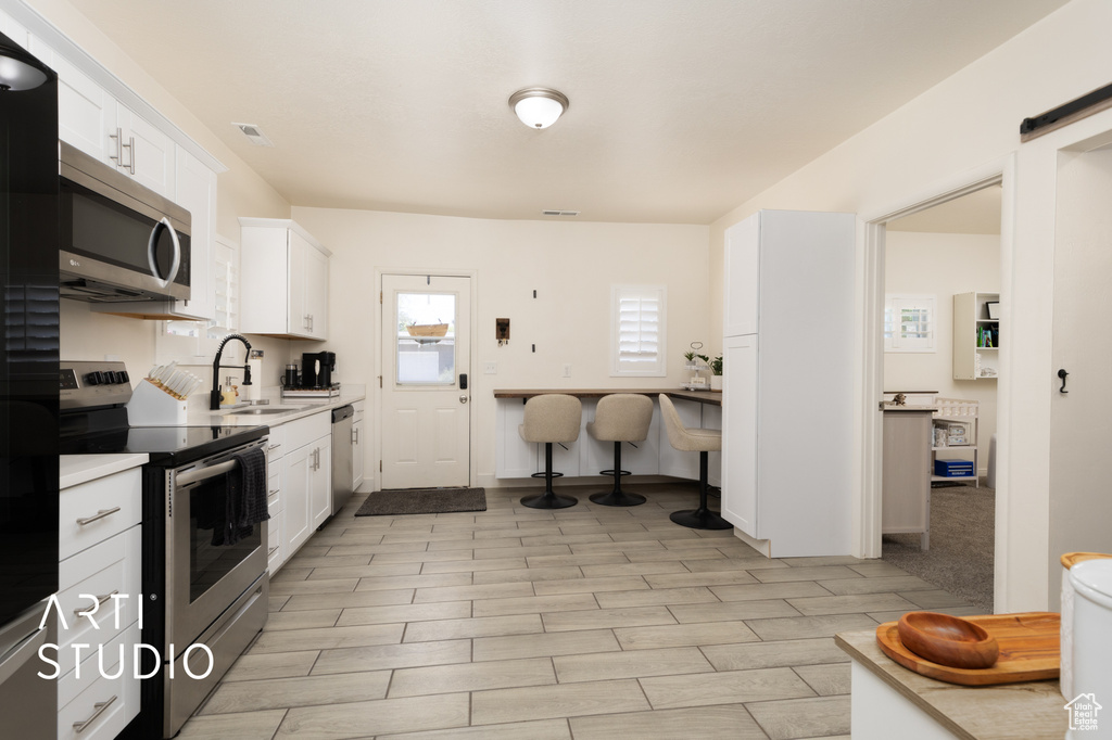Kitchen with stainless steel appliances, a sink, white cabinets, and light countertops