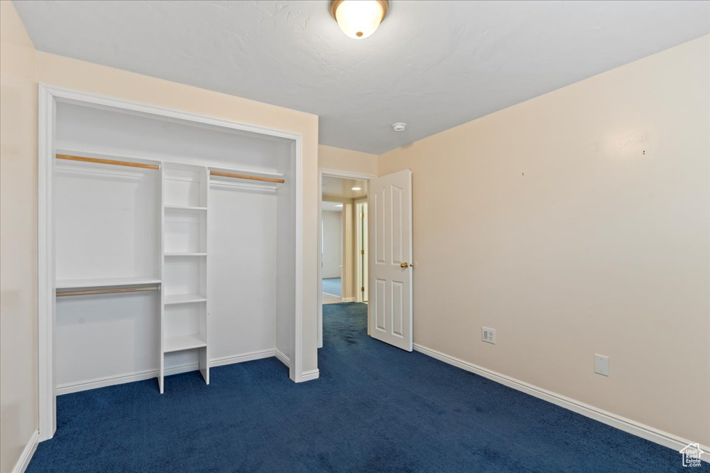 Unfurnished bedroom with dark carpet, baseboards, and a closet