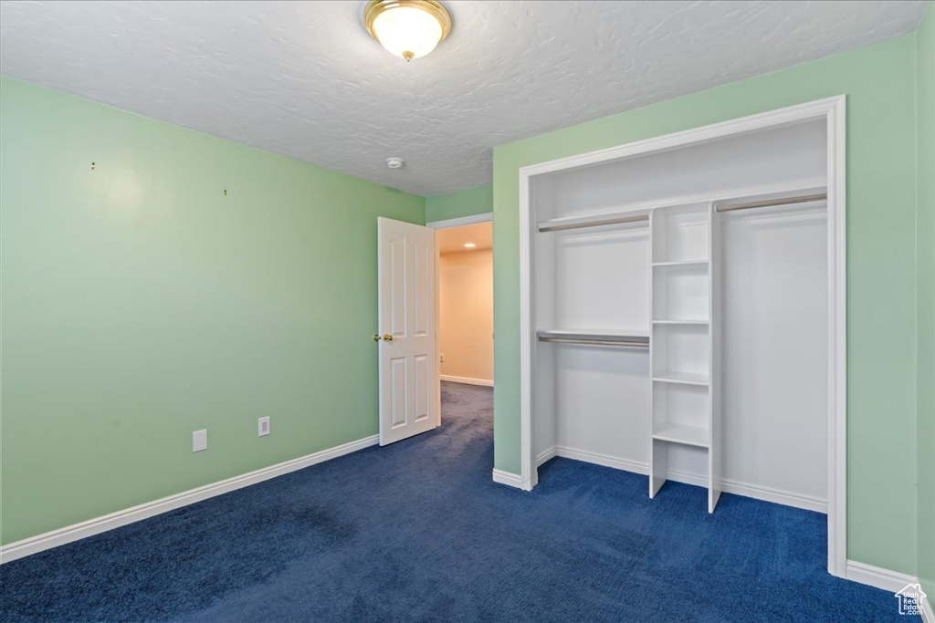 Unfurnished bedroom with dark carpet, baseboards, a textured ceiling, and a closet