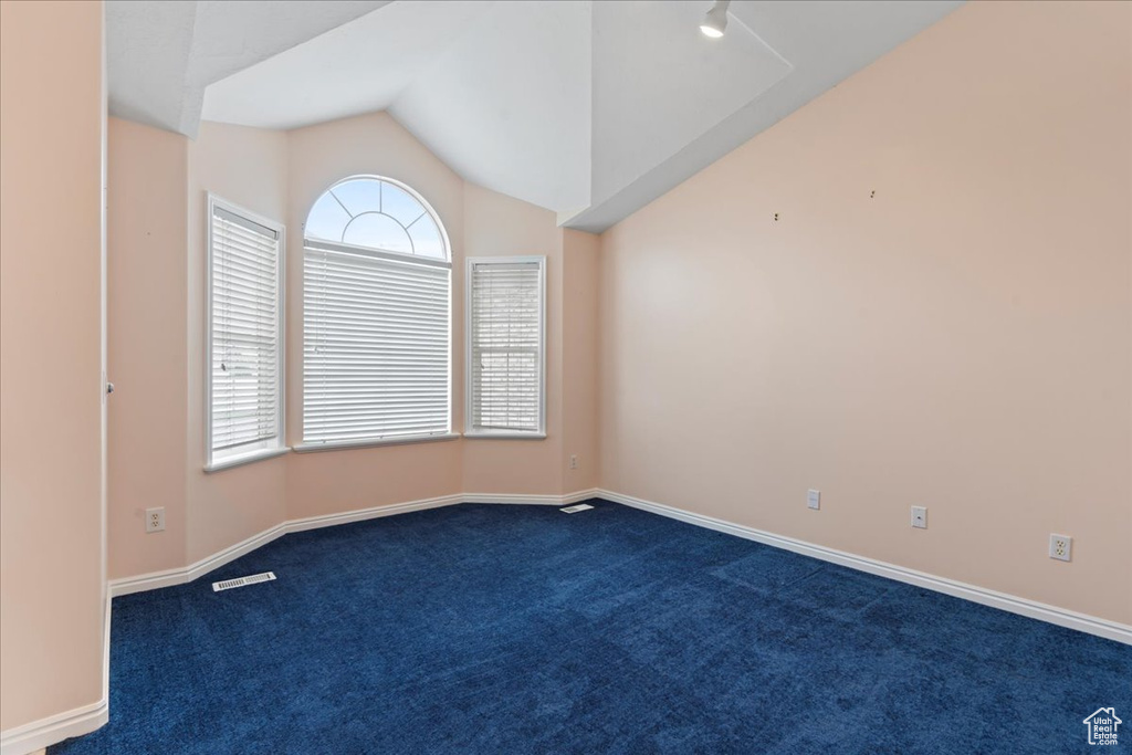 Empty room with dark carpet, lofted ceiling, and baseboards