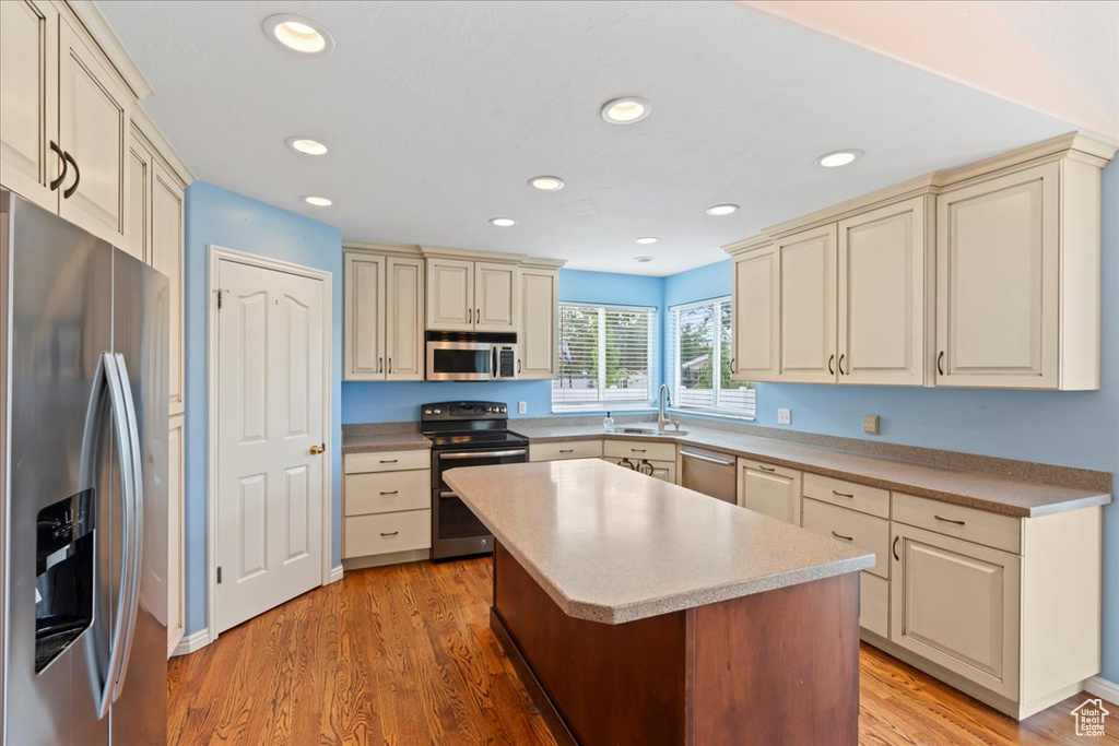 Kitchen with stainless steel appliances, cream cabinets, a sink, light wood-type flooring, and recessed lighting