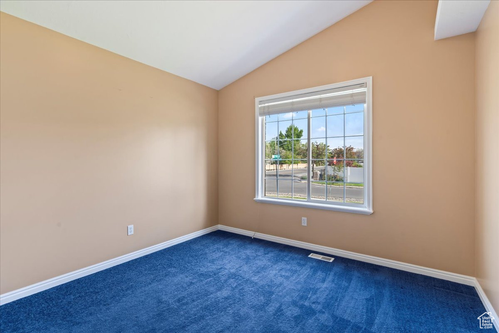 Spare room with dark colored carpet, baseboards, and lofted ceiling