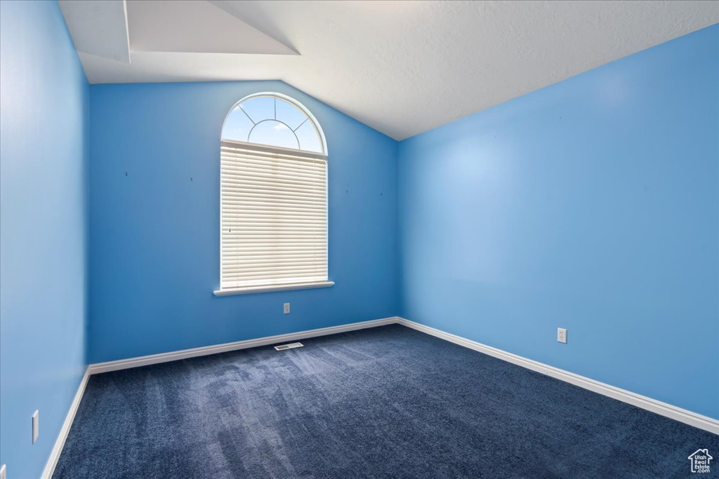 Empty room featuring vaulted ceiling, dark carpet, and baseboards