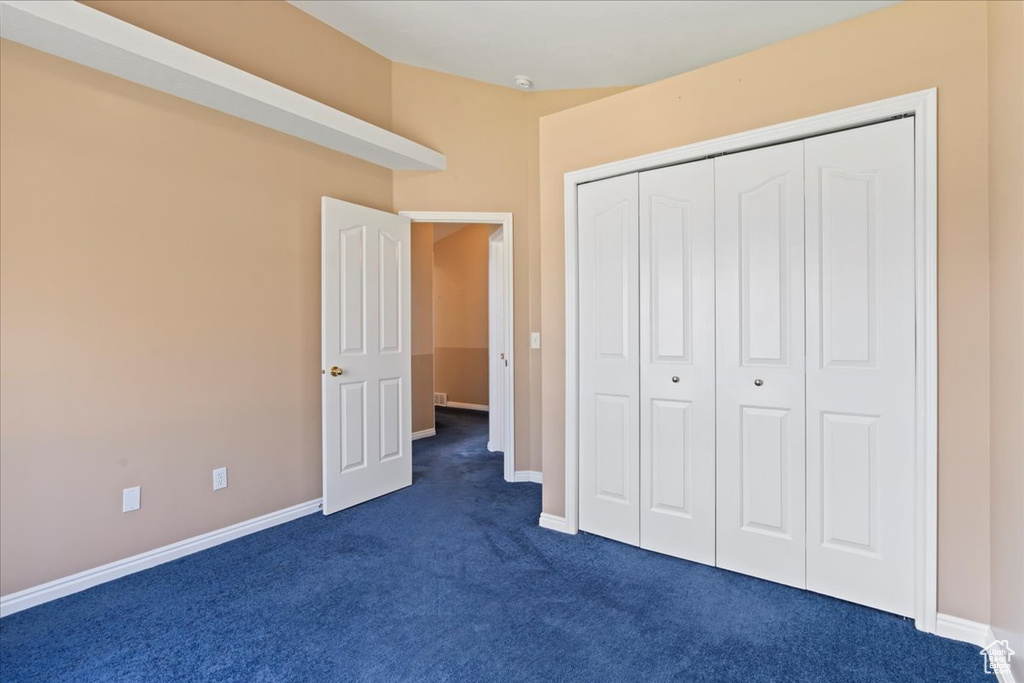 Unfurnished bedroom with dark colored carpet, a closet, and baseboards